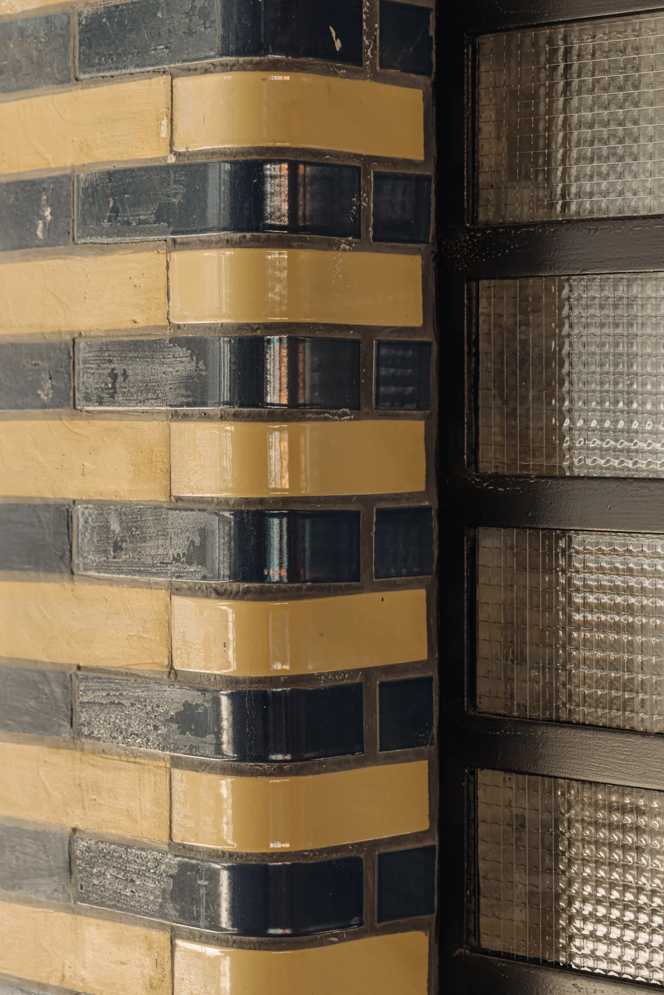 Detail van een gebogen hoek van een gevel aan de Muntkade met glanzende geel-blauwe bakstenen en glasbouwstenen.