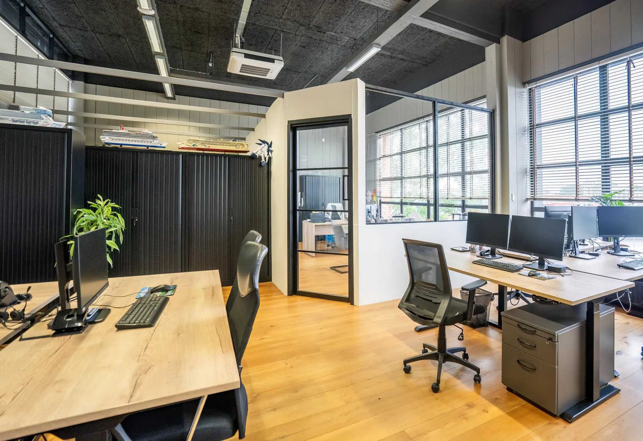 Modern kantoorinterieur aan de Schiedamsedijk met houten vloeren, werkplekken en grote ramen met jaloezieën.