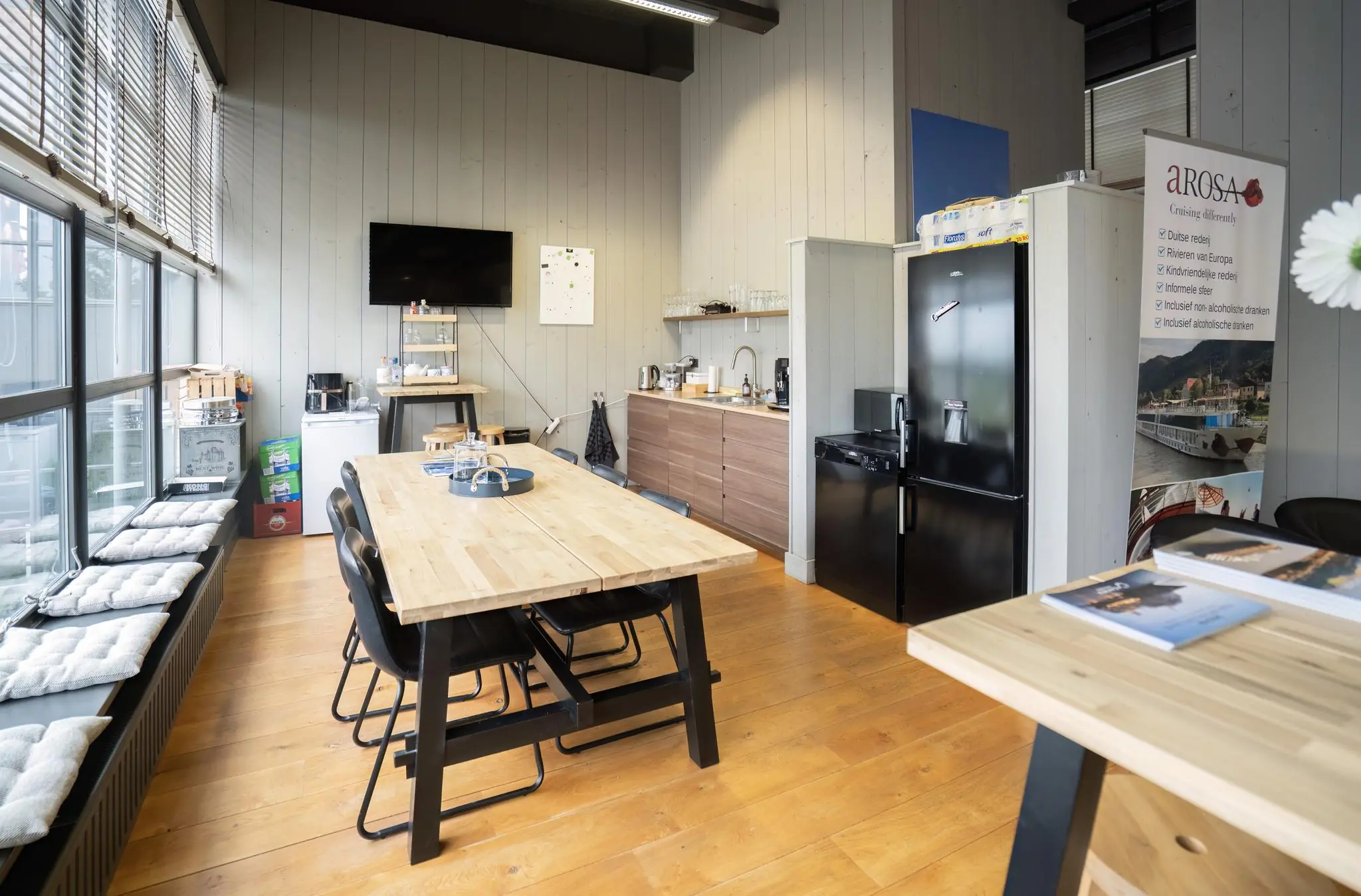 Moderne kantineruimte aan de Schiedamsedijk met houten vloer, grote ramen, keukenhoek en vergadertafel.