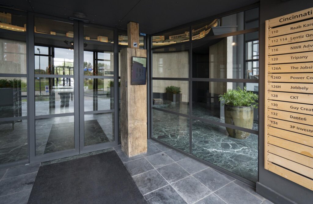 Ingang van een modern kantoorgebouw aan de Schiedamsedijk met glazen draaideur en bedrijvenbord.