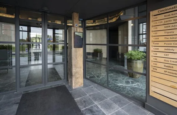 Ingang van een modern kantoorgebouw aan de Schiedamsedijk met glazen draaideur en bedrijvenbord.