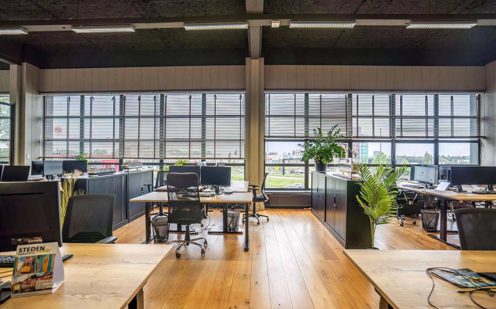 Modern kantoorinterieur aan de Schiedamsedijk met houten vloer, open werkplekken en grote ramen met jaloezieën.