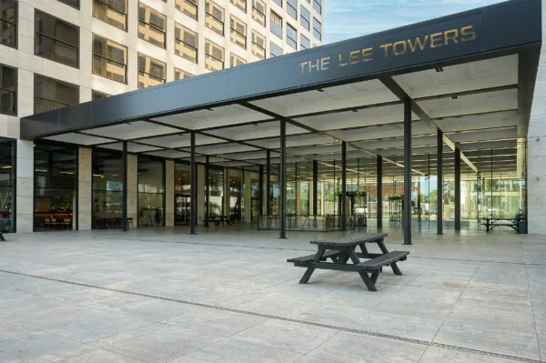 Ingang van The Lee Towers aan de Galvanistraat met glazen gevel, overkapping en picknicktafels op het plein.