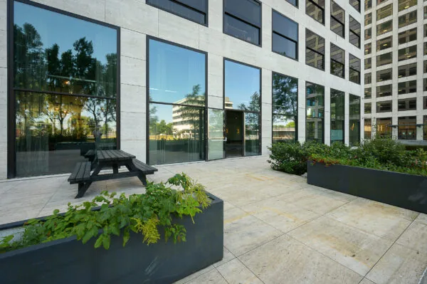 Moderne kantoorgevel aan de Galvanistraat met grote ramen, plantenbakken en een picknicktafel op een betegeld terras.
