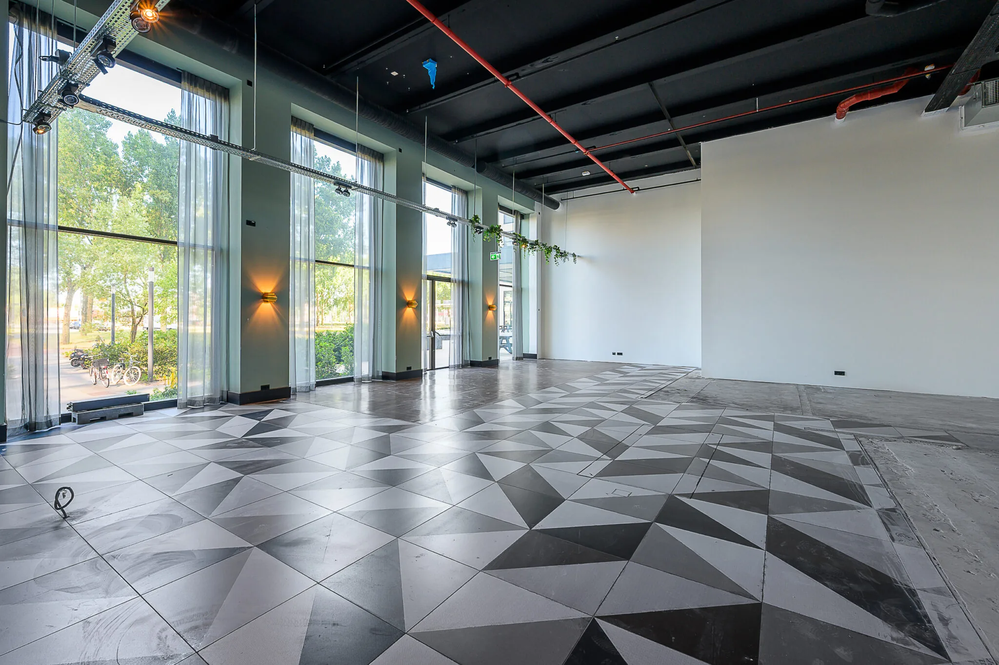 Lichte, moderne ruimte aan de Galvanistraat met hoge ramen, zwart plafond en geometrisch betegelde vloer.