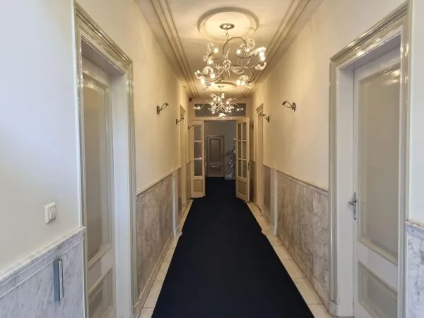 Verlichtte klassieke gang met marmeren lambrisering en open dubbele deuren in een pand aan het Lange Voorhout.