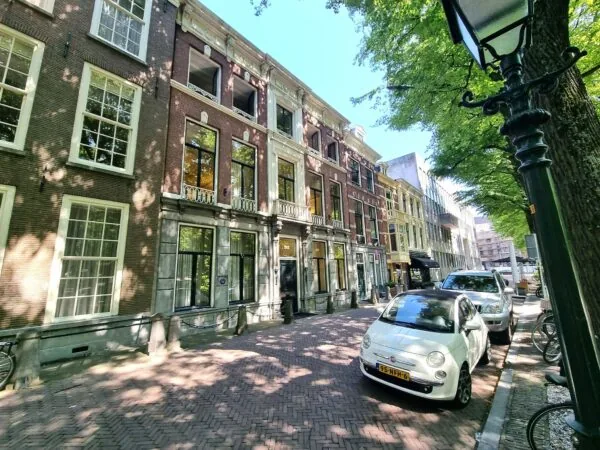 Gevels van historische panden aan het Lange Voorhout in Den Haag, met geparkeerde auto's en schaduwrijke bomen.