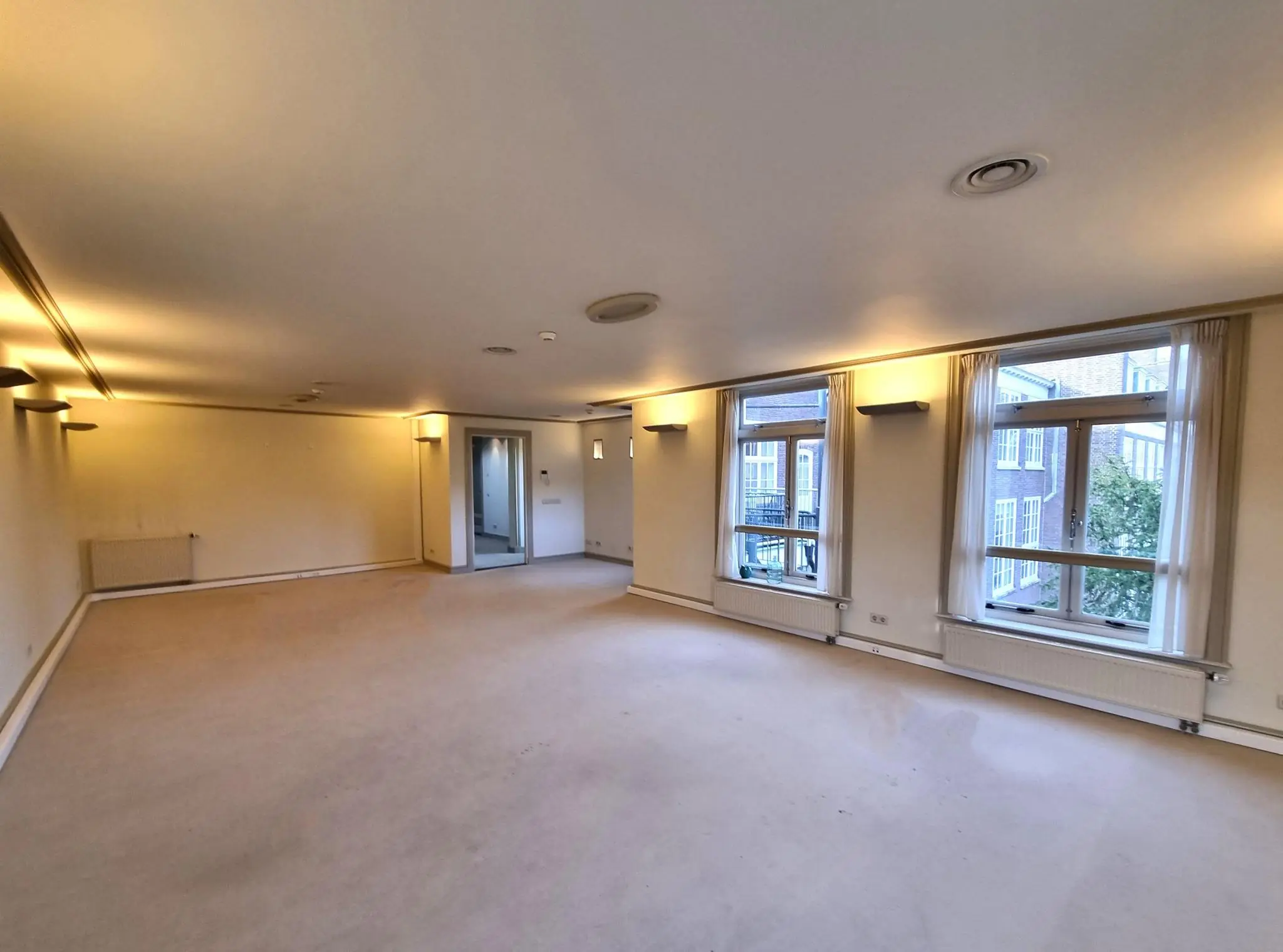 Ruime, leegstaande woonkamer met grote ramen en uitzicht op het Lange Voorhout.