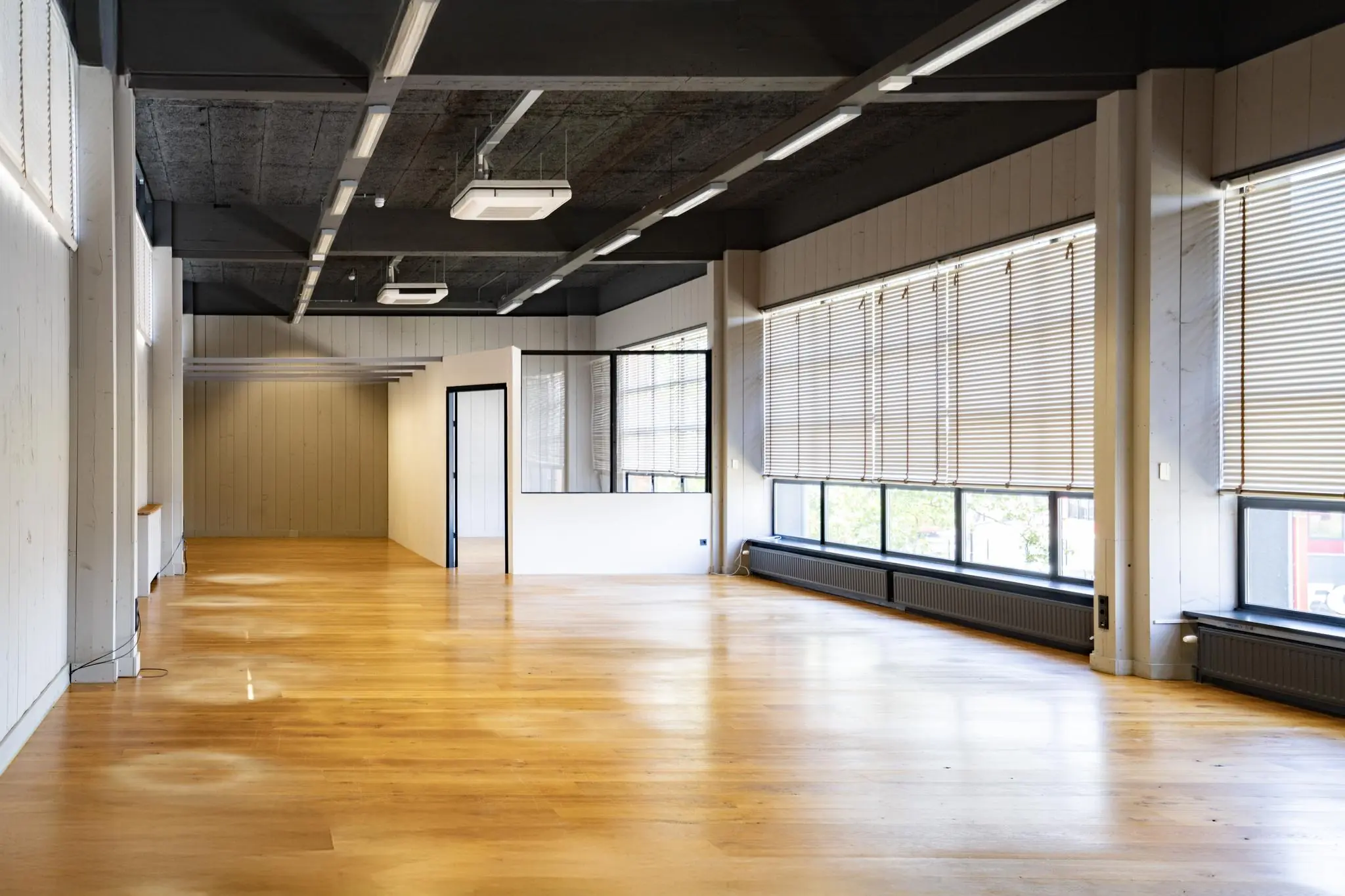 Licht en modern kantoorinterieur aan de Schiedamsedijk met houten vloer, grote ramen en zonwering.