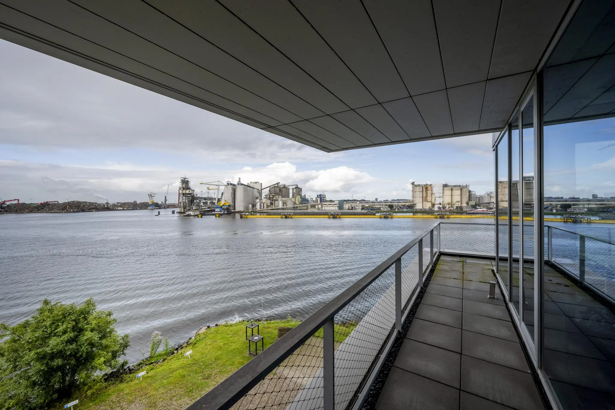 Uitzicht vanaf een balkon aan de Moermanskkade op een industriële kade aan het water met silo’s en kranen.