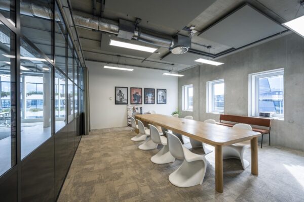 Vergaderruimte aan de Moermanskkade met een lange houten tafel, moderne witte stoelen, industriële plafonddetails en kunst aan de muur.