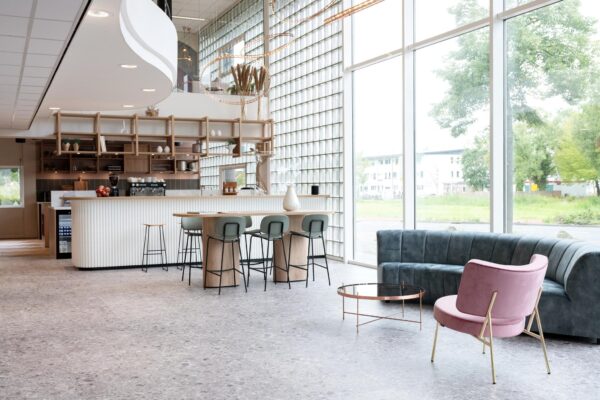 Moderne en lichte lounge- en koffiehoek in een interieur aan de Overschiestraat met grote ramen en stijlvol meubilair.