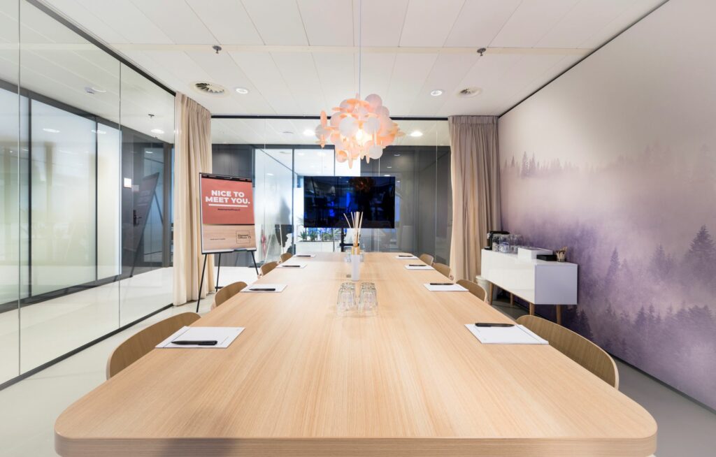 Moderne vergaderruimte met een lange houten tafel, notitieblokken, een decoratieve hanglamp en een muurprint van een mistig bos.