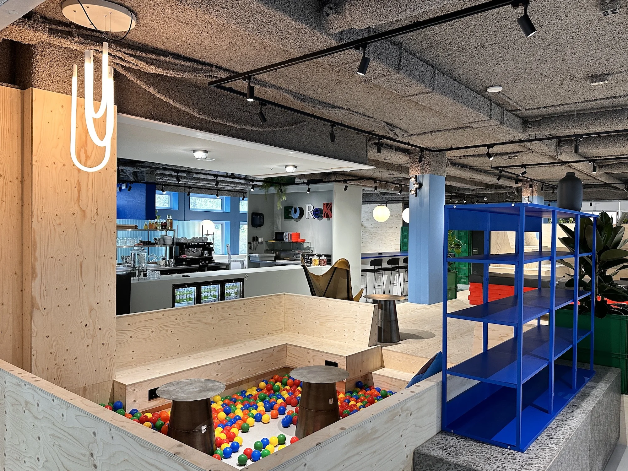 Moderne kantoorlounge aan de Daltonlaan met een koffiebalie, ballenbak en felblauwe stellingkast.