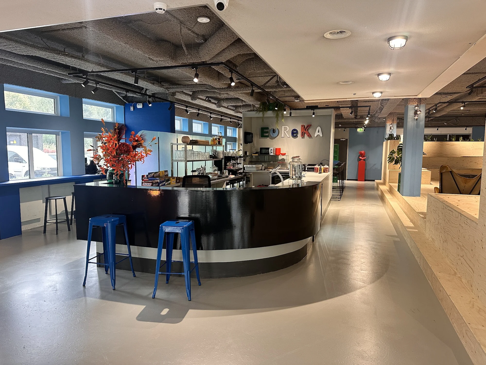 Moderne, kleurrijke koffieruimte met een zwarte bar en de tekst "EUREKA" aan de muur in een bedrijfsruimte aan de Daltonlaan.