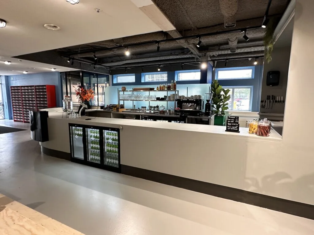 Moderne koffiebar met een strakke witte balie en een volledig uitgeruste achterwand in een kantoorruimte aan de Daltonlaan.