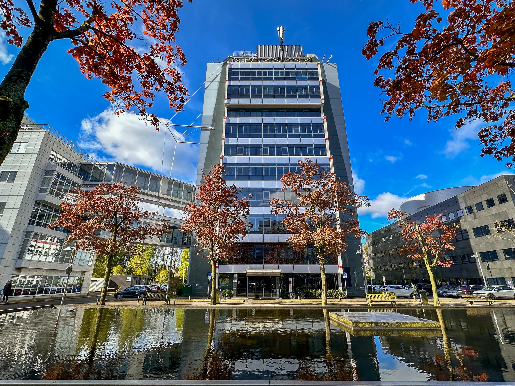 Kantoorgebouw aan de Daltonlaan in Utrecht, weerspiegeld in een vijver met herfstkleurige bomen op de voorgrond.