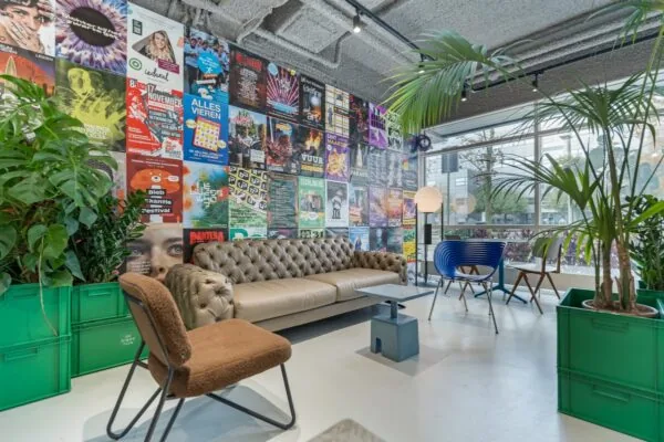 Hip ingerichte loungehoek met een leren bank, kleurrijke stoelen, veel planten en een muur vol posters in een modern kantoor aan de Daltonlaan.