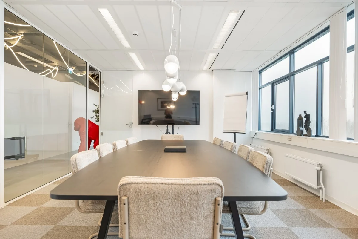 Vergaderruimte aan de Daltonlaan met een lange tafel, moderne stoelen, een groot scherm, en glazen wanden.