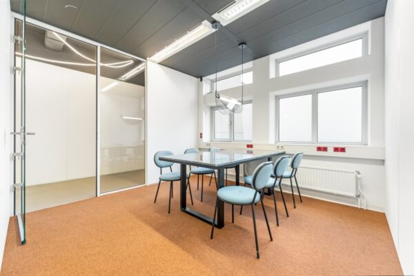 Vergaderruimte aan de Daltonlaan met glazen wanden, moderne verlichting, en een tafel met zes lichtblauwe stoelen.