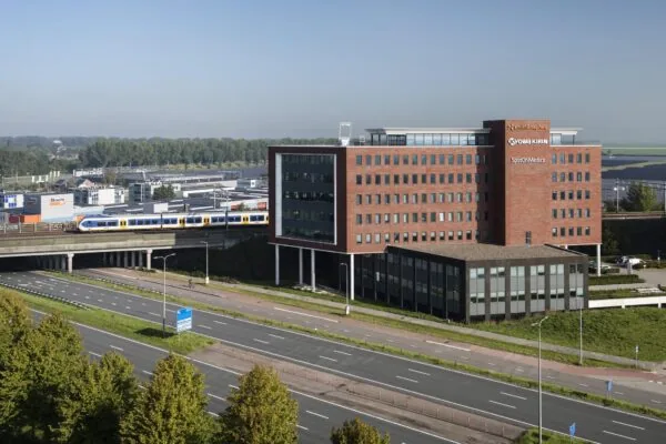 Kantoorgebouw met de namen Smith & Nephew, Kyowa Kirin en SpotOnMedics langs een snelweg en spoorlijn waar een trein voorbijrijdt.