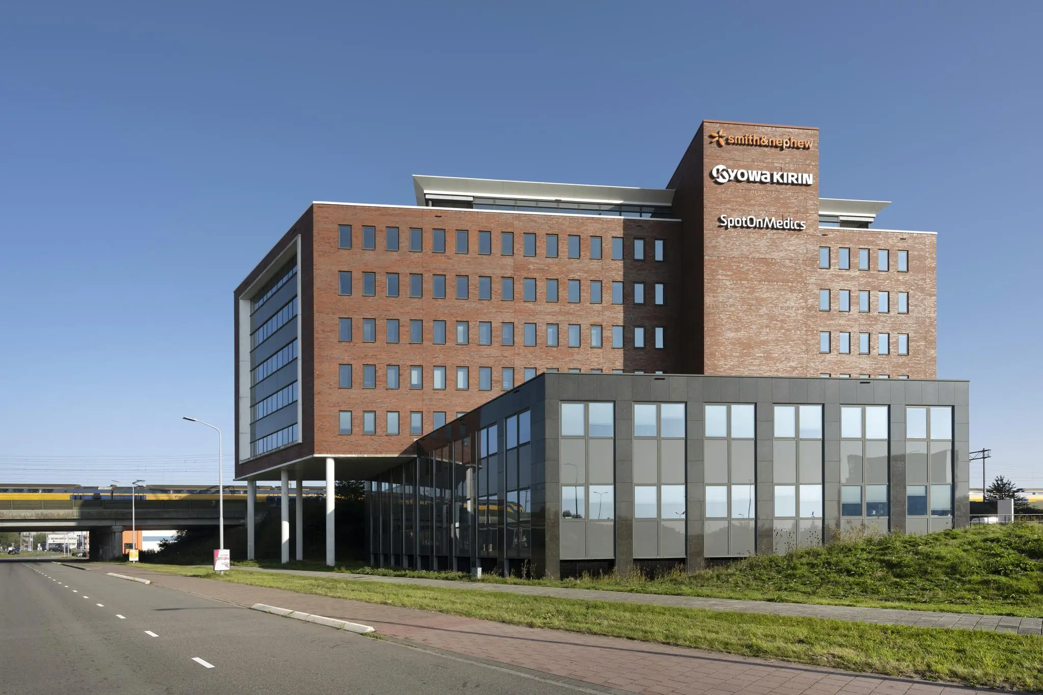 Kantoorgebouw met de logo’s van Smith & Nephew, Kyowa Kirin en SpotOnMedics langs een weg en spoorlijn.