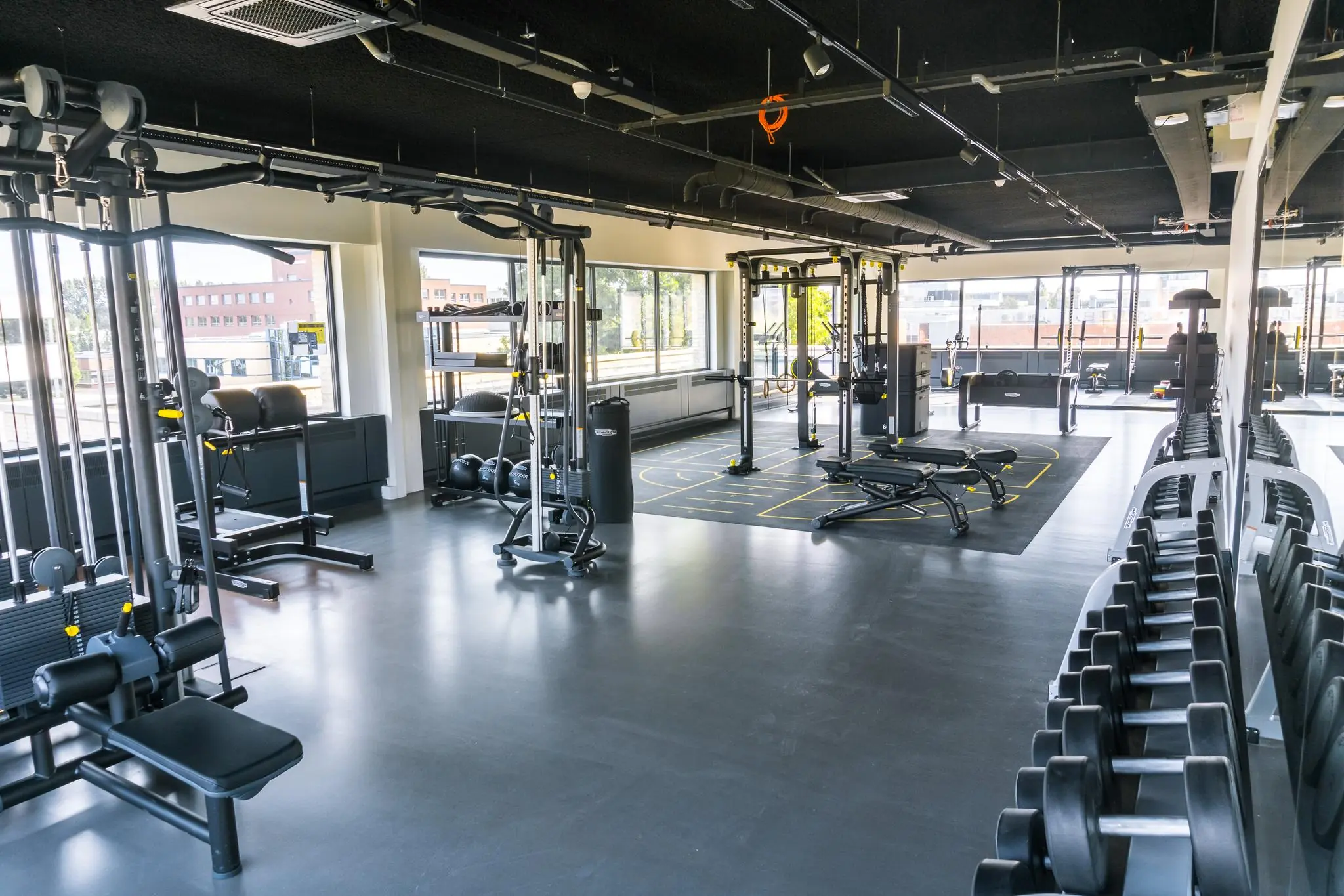 Moderne en ruime fitnessruimte met diverse krachttrainingsapparaten, gewichten en functionele trainingszones.