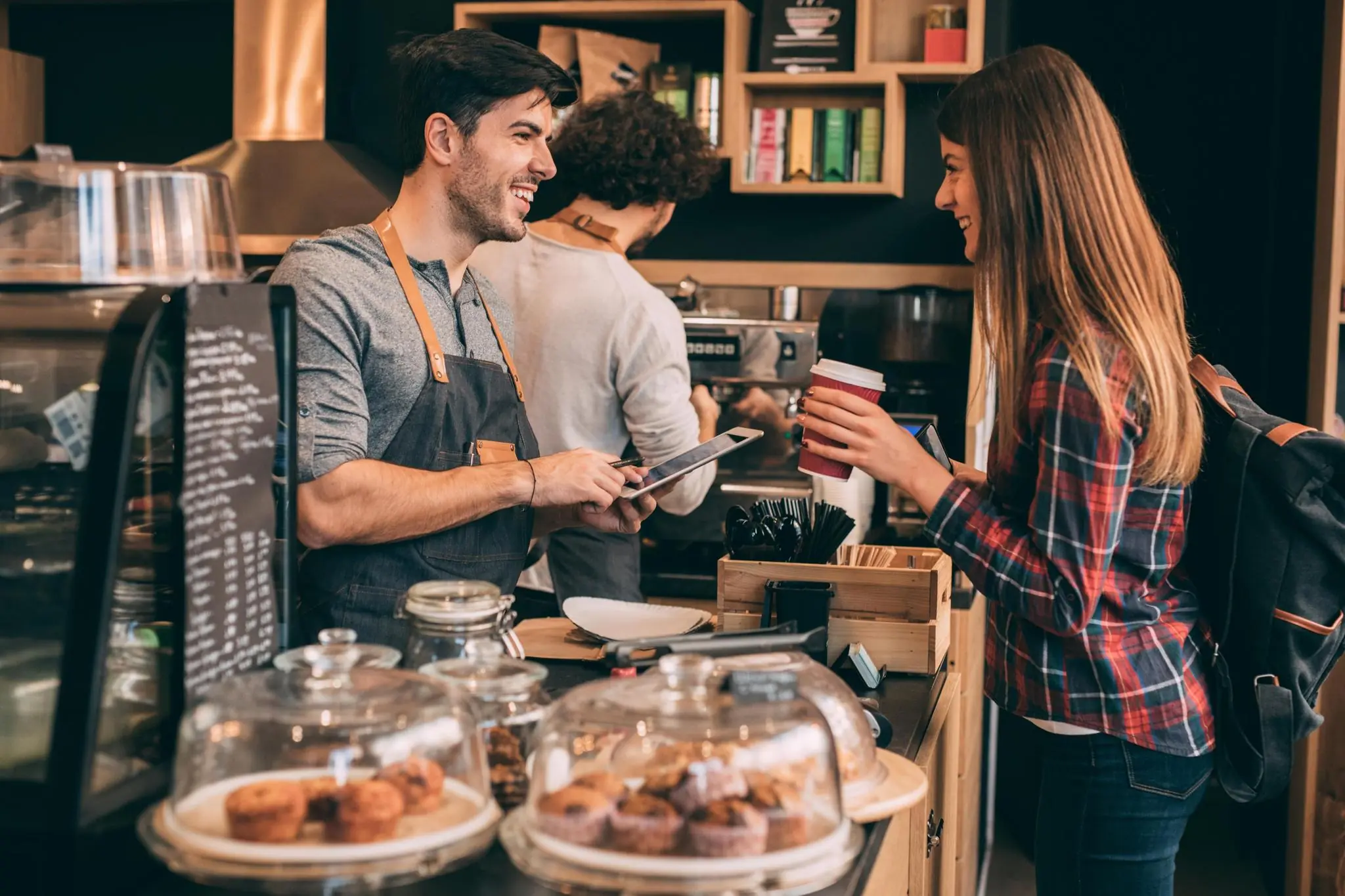 Vriendelijke barista helpt klant met een koffiebeker aan de toonbank van een gezellige koffiebar.
