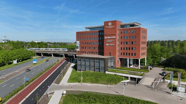 Kantoorgebouw 'The Botanic Offices' met bedrijfslogo's op de gevel, gelegen naast een spoorviaduct en autoweg.
