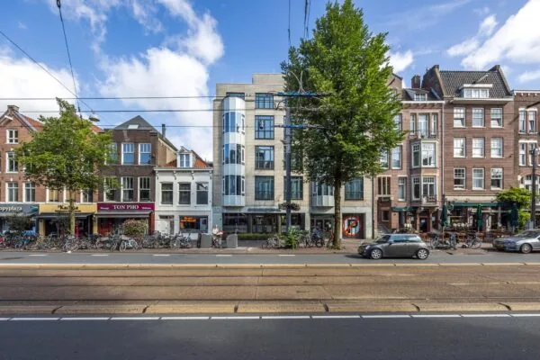 Winkel- en woonpanden aan de Overtoom in Amsterdam met geparkeerde fietsen en passerende auto's.