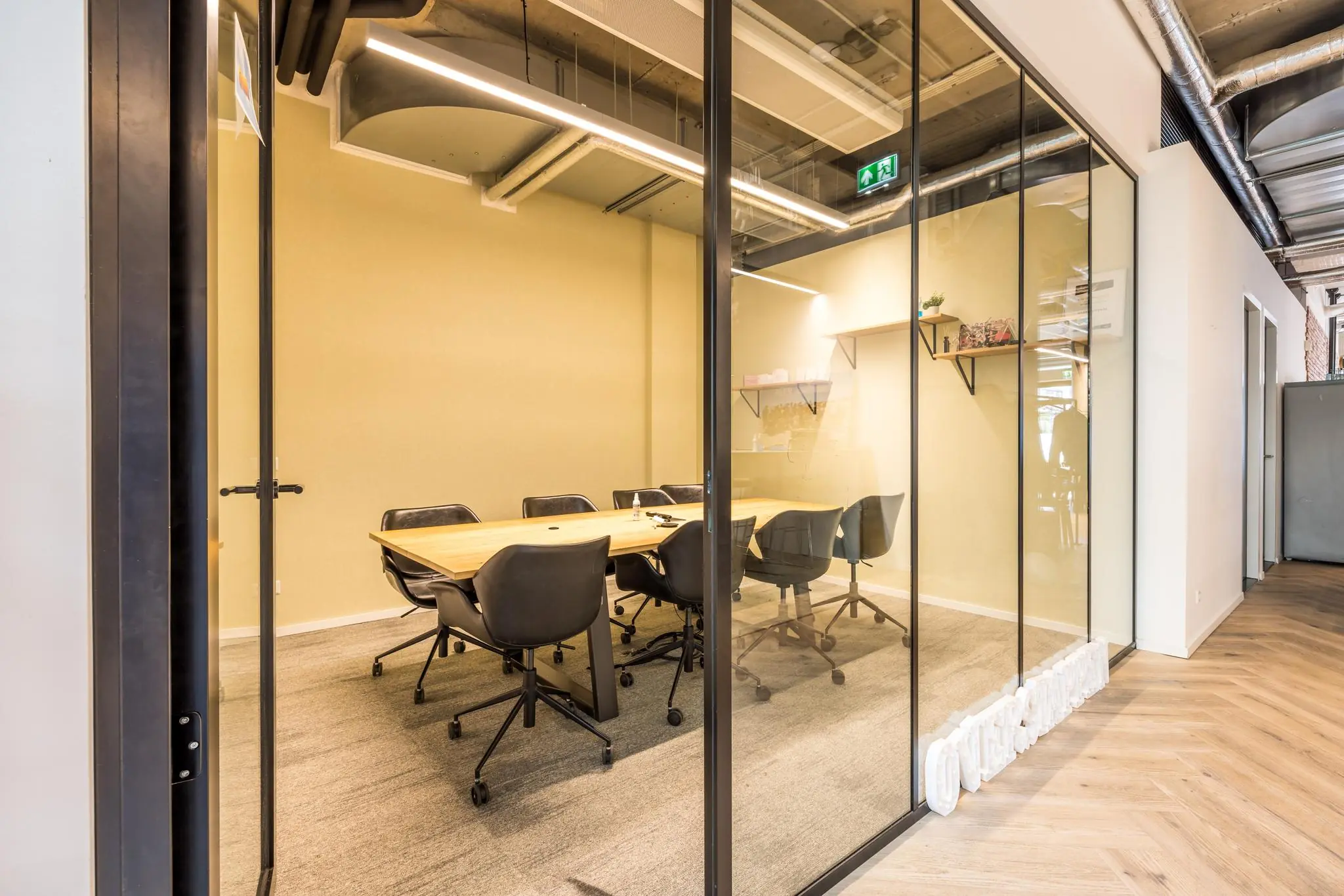 Vergaderruimte met glazen wanden, houten tafel en zwarte stoelen in kantoorpand aan de Overtoom.
