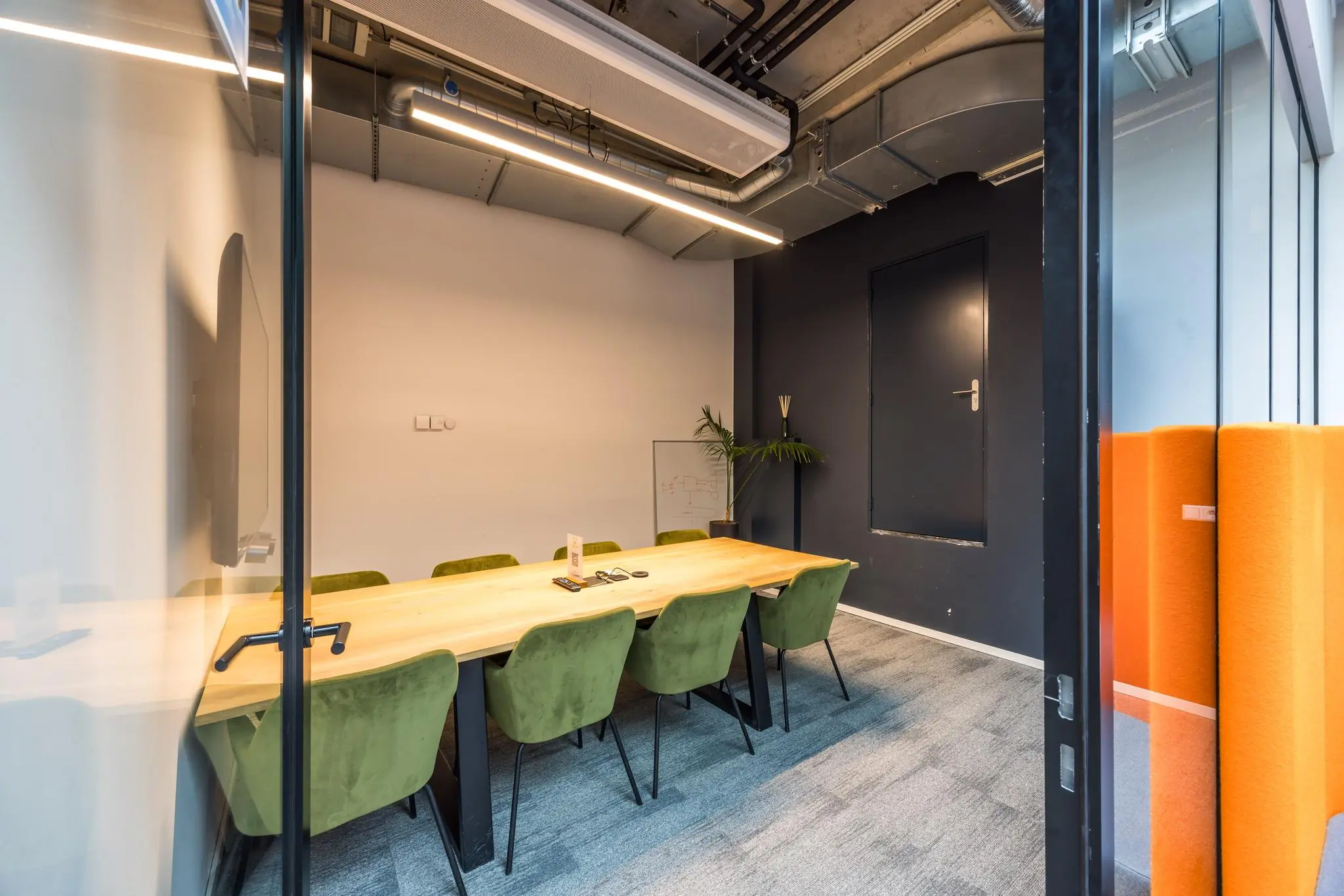 Vergaderruimte Overtoom met een houten tafel, groene stoelen en industriële plafondafwerking.