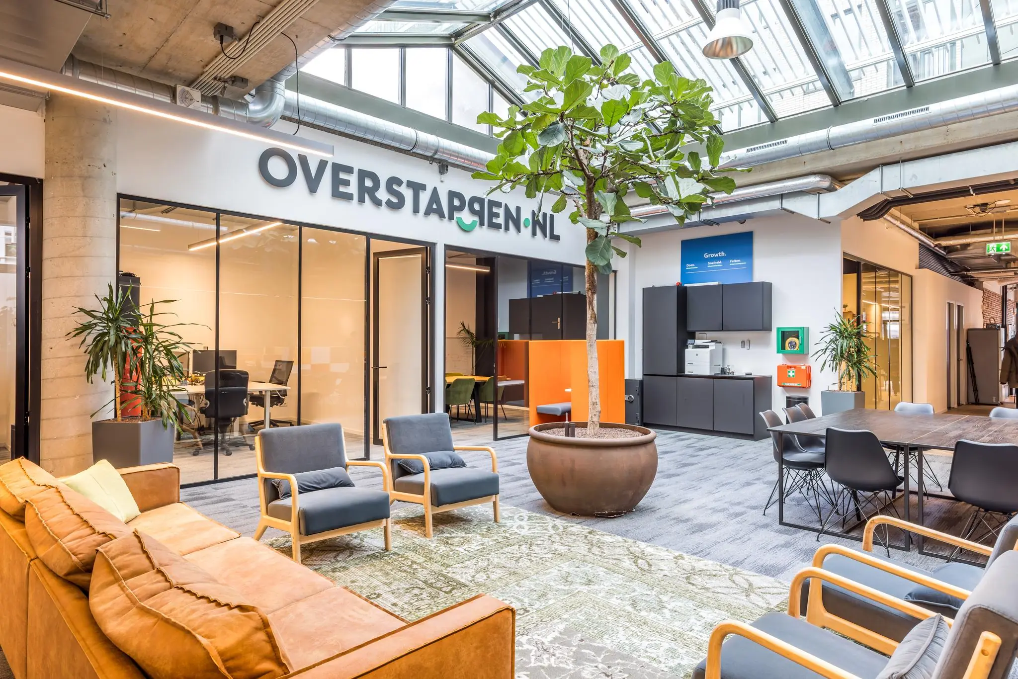 Moderne en lichte kantoorruimte van Overstappen.nl met zithoeken, werkplekken en een grote binnentuinplant.