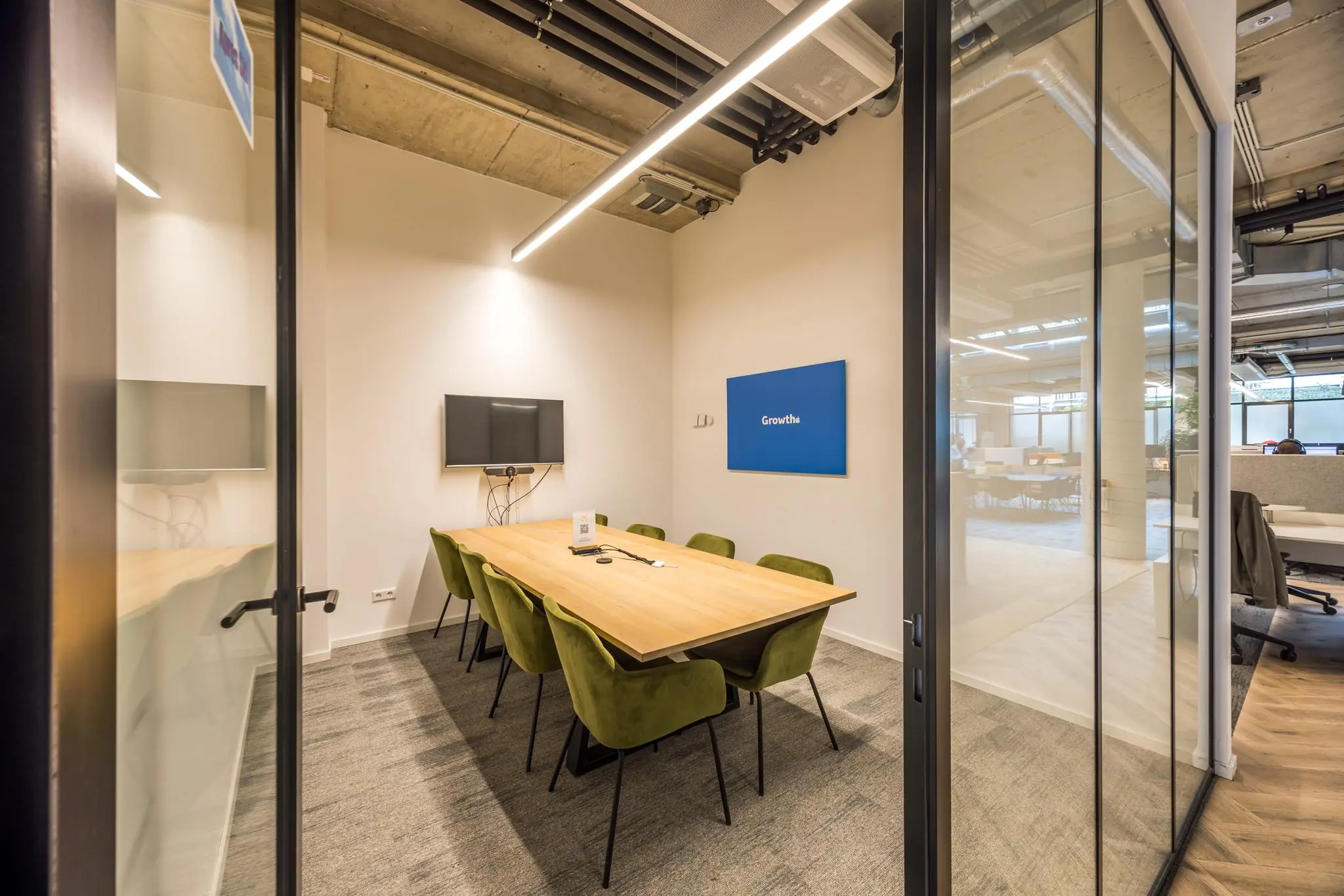 Vergaderruimte met houten tafel, groene stoelen, flatscreen en een blauw bord met de tekst "Growth" aan de muur.