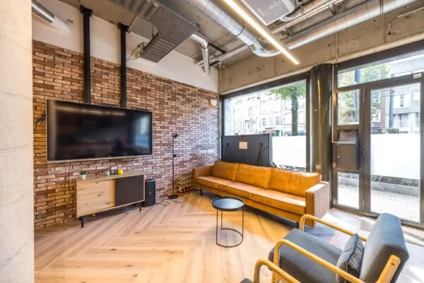 Moderne loungehoek aan de Overtoom met grote tv, leren bank, industriële accenten en zicht op de straat.