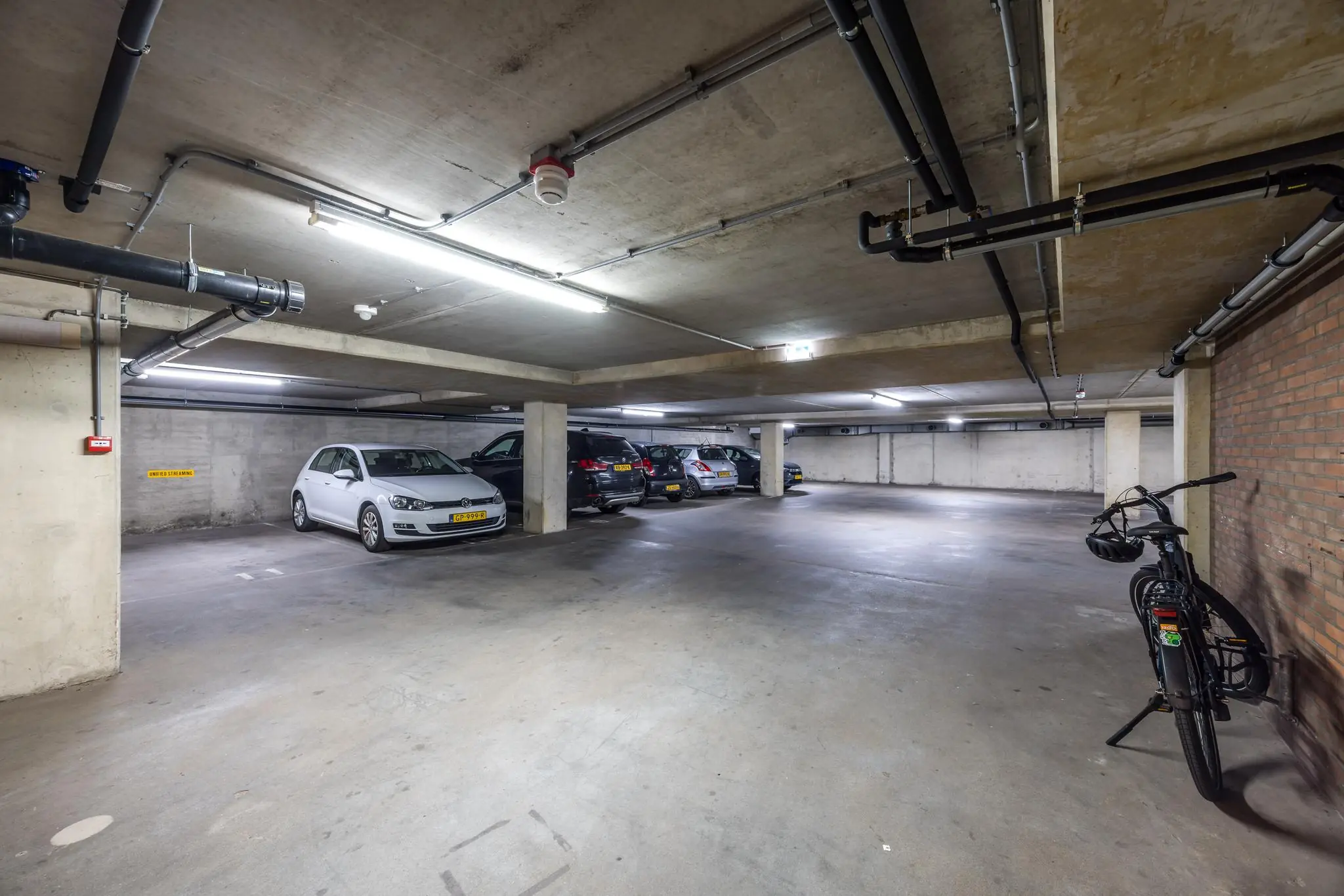 Ondergrondse parkeergarage Overtoom met geparkeerde auto's en een fiets tegen een bakstenen muur.
