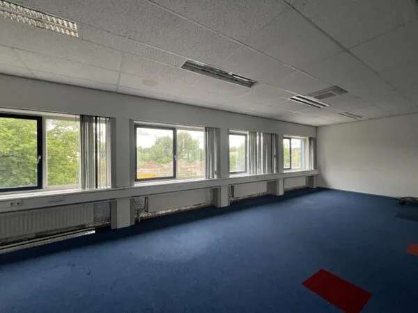 Licht kantoorruimte aan de 2e Daalsedijk met blauwe vloerbedekking, grote ramen en systeemplafond.