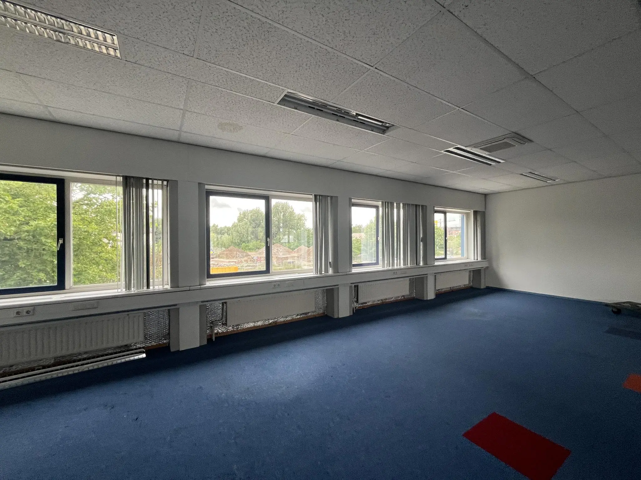 Licht kantoorruimte aan de 2e Daalsedijk met blauwe vloerbedekking, grote ramen en systeemplafond.