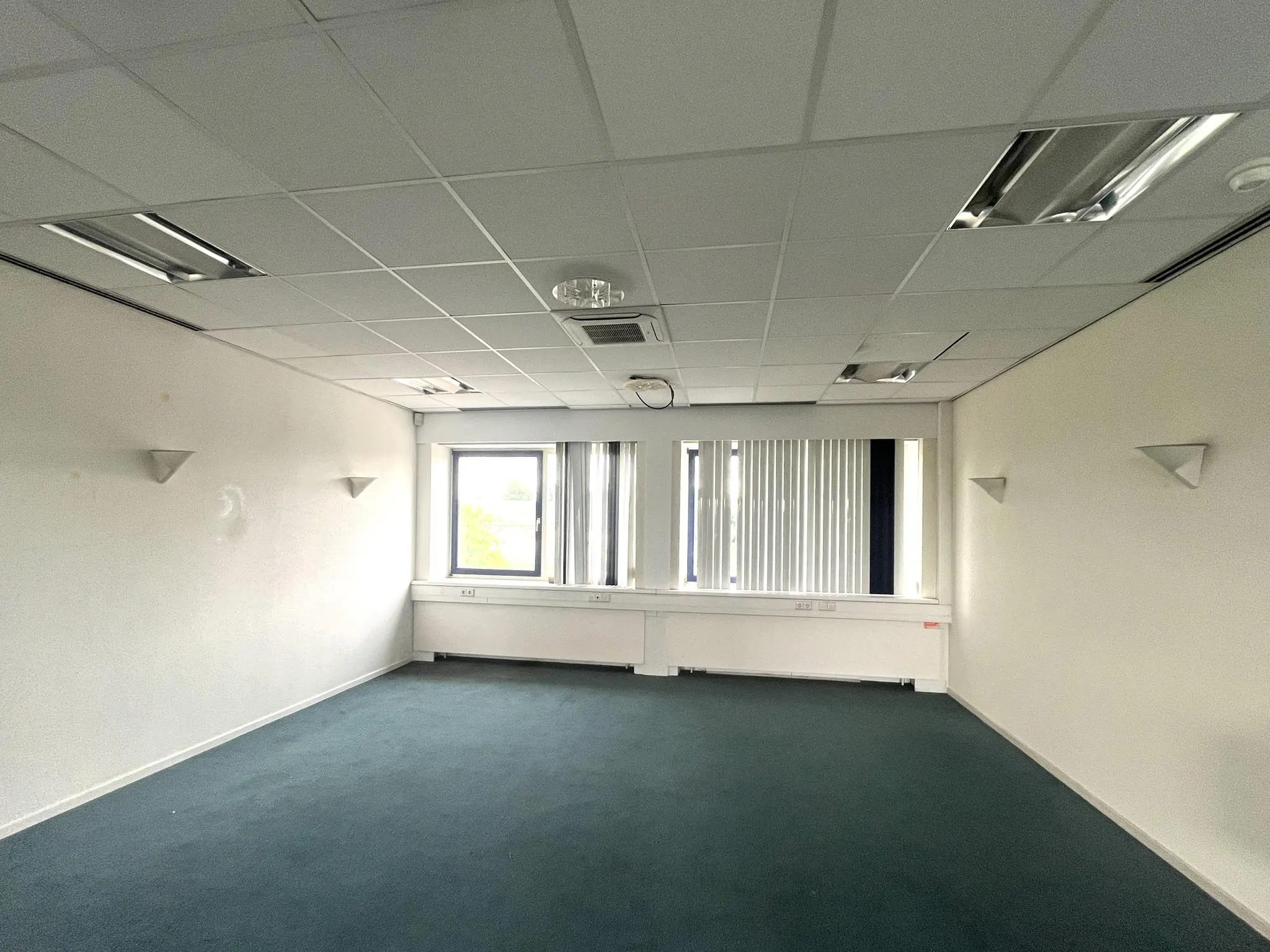 Leeg kantoorpand aan de 2e Daalsedijk met witte muren, systeemplafond en verticale lamellen voor het raam.