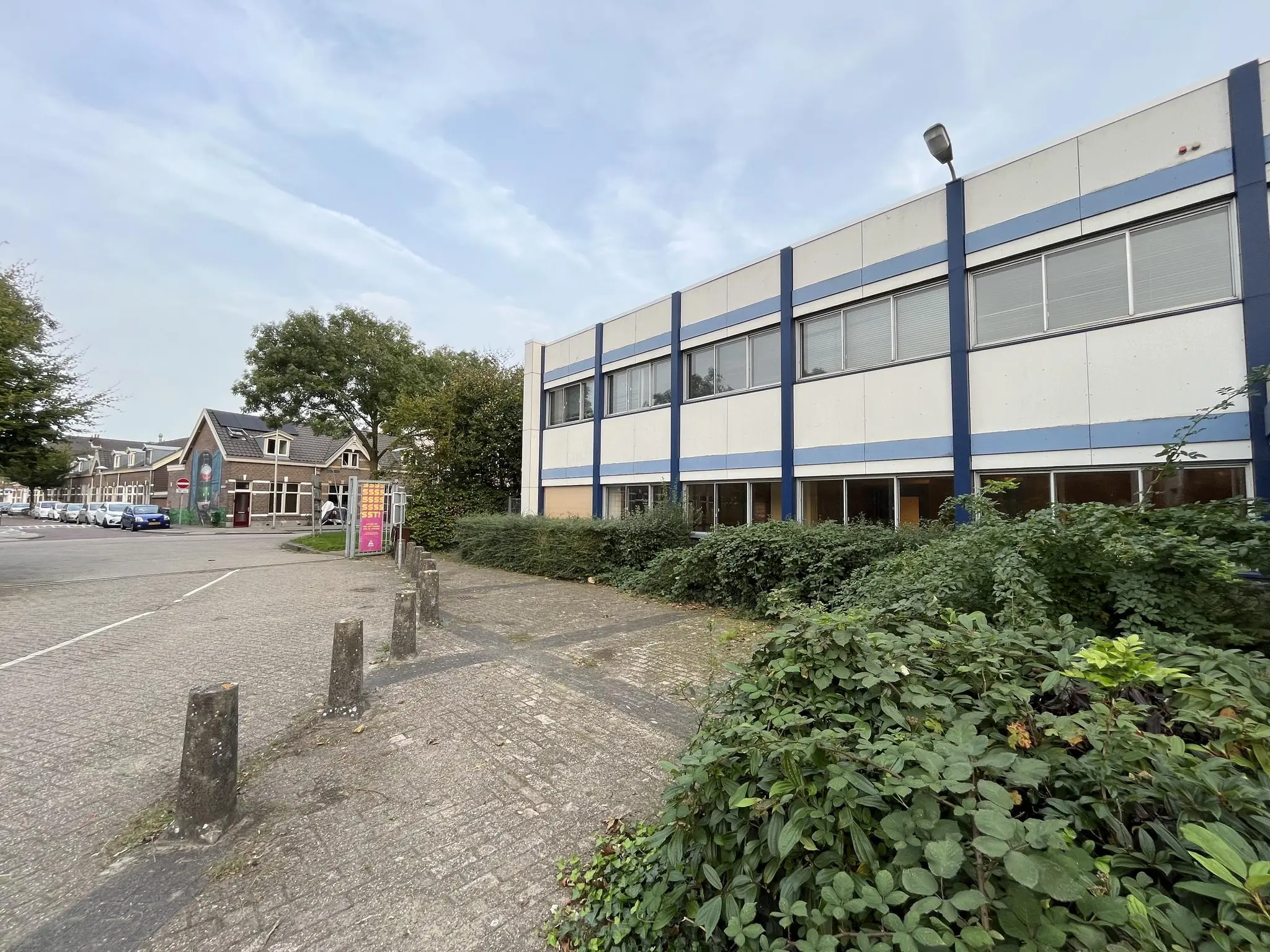 Straatbeeld van de 2e Daalsedijk met een kantoorpand met blauwe gevelstroken en een woonhuis op de achtergrond.