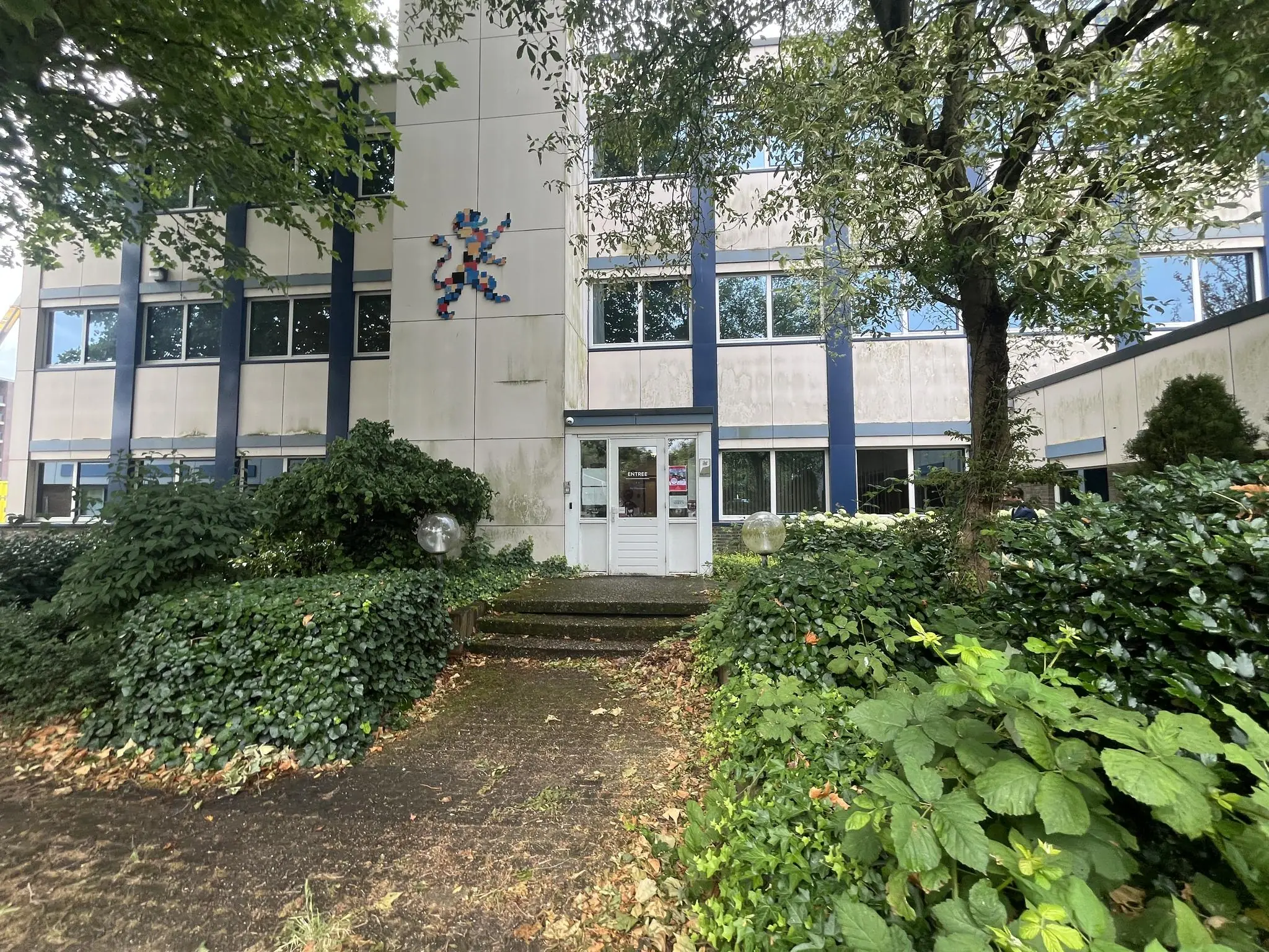 Vooraanzicht van een kantoorgebouw aan de 2e Daalsedijk, omgeven door groen met een kleurrijk mozaïek op de gevel.