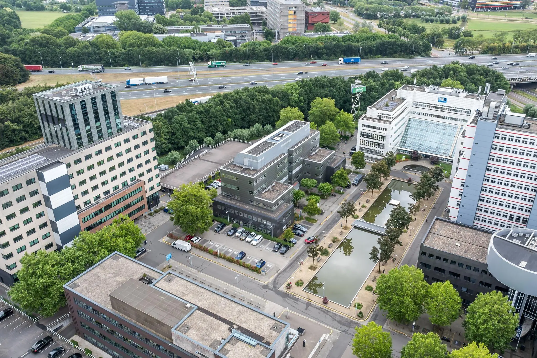 Luchtfoto van kantorencomplex aan de Daltonlaan in Utrecht met omliggende gebouwen, vijvers en snelweg op de achtergrond.
