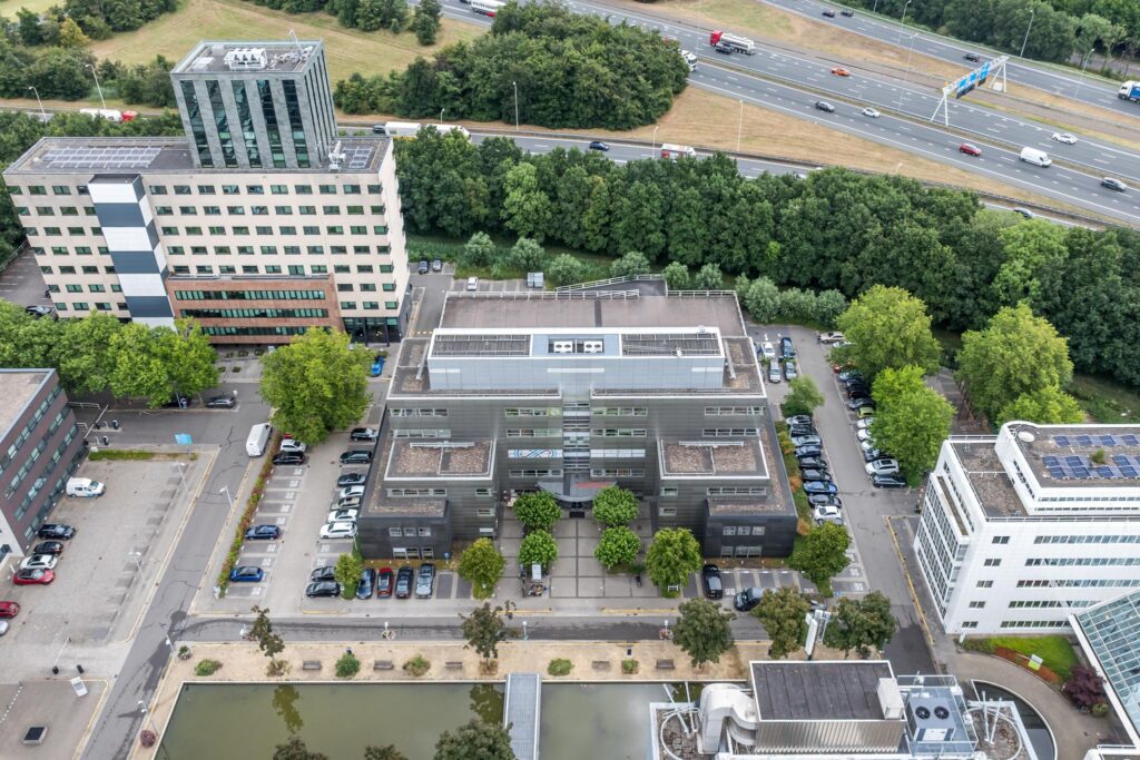 Luchtfoto van een kantoorgebouw aan de Daltonlaan in Utrecht, omringd door parkeerplaatsen, andere gebouwen en een snelweg op de achtergrond.
