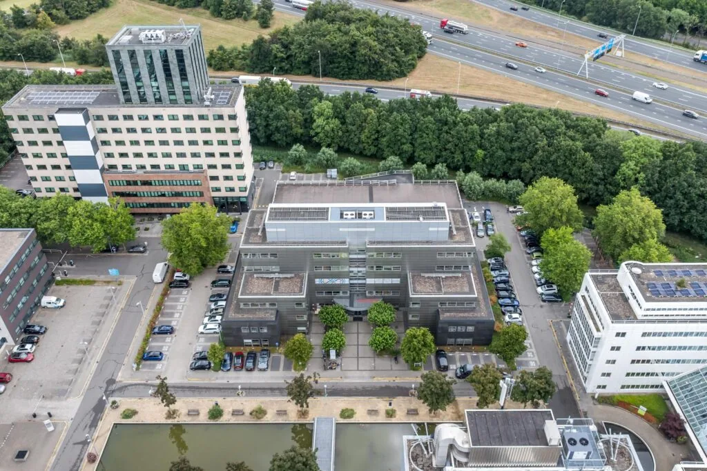 Luchtfoto van een kantoorgebouw aan de Daltonlaan in Utrecht, omringd door parkeerplaatsen, andere gebouwen en een snelweg op de achtergrond.