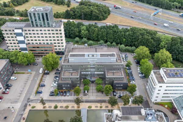 Luchtfoto van een kantoorgebouw aan de Daltonlaan in Utrecht, omringd door parkeerplaatsen, andere gebouwen en een snelweg op de achtergrond.