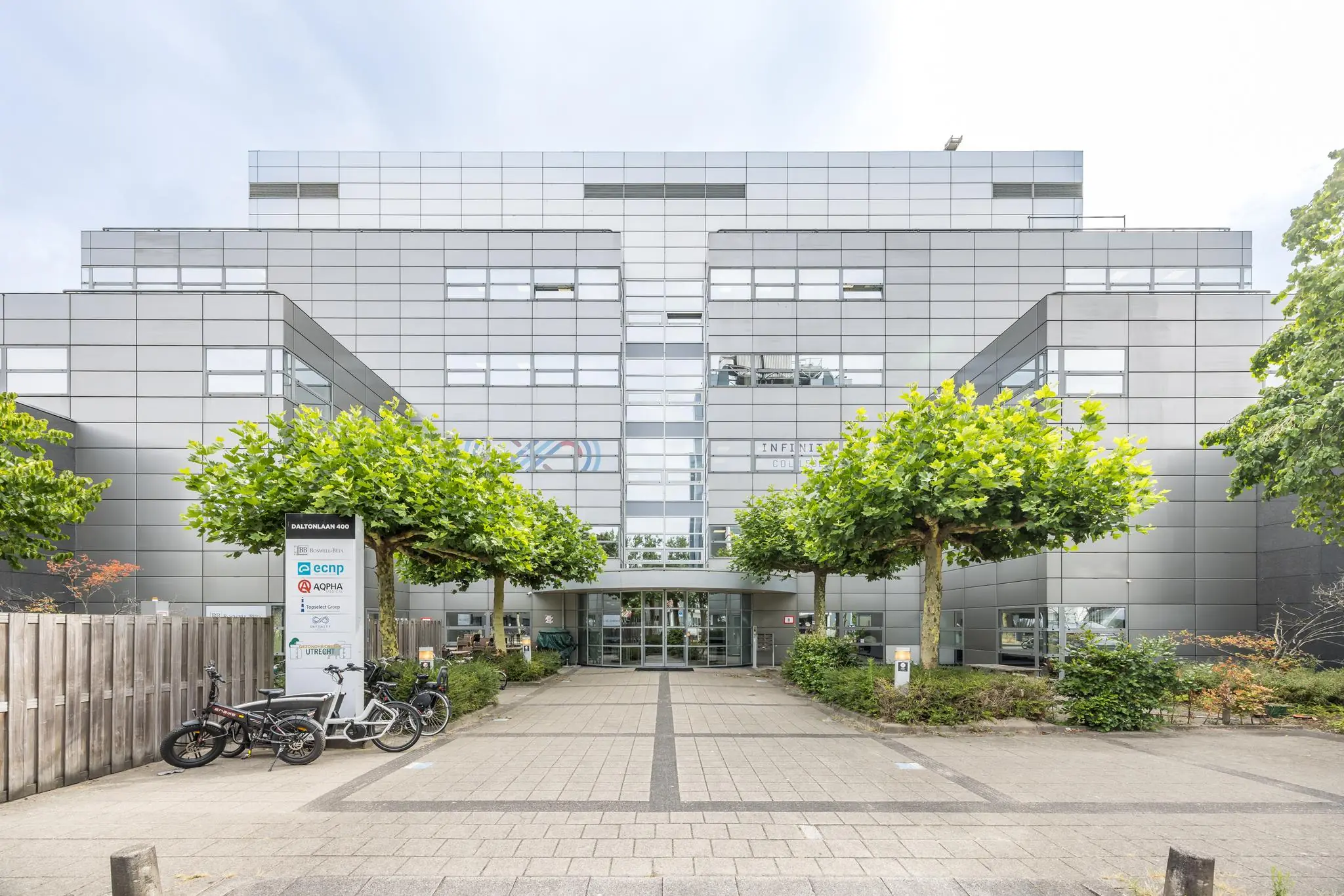 Ingang van een modern kantoorgebouw aan de Daltonlaan 400 in Utrecht, omgeven door jonge bomen en fietsenrekken.