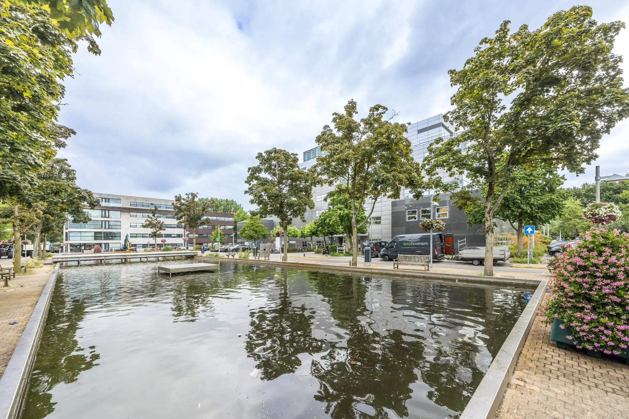 Vijver met omringende bomen en moderne kantoorgebouwen aan de Daltonlaan in een stedelijke omgeving.