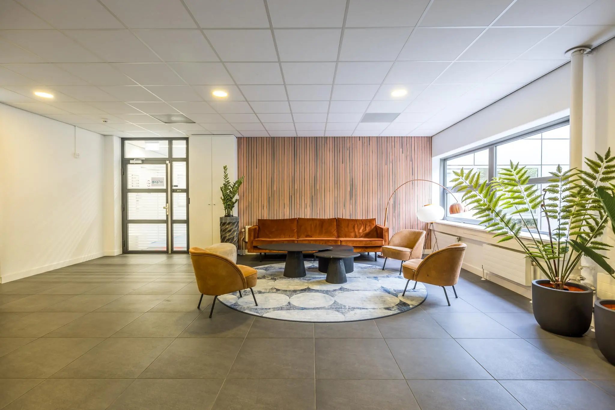 Moderne wachtruimte aan de Daltonlaan met retro meubels, houten wandpanelen en grote raampartij.