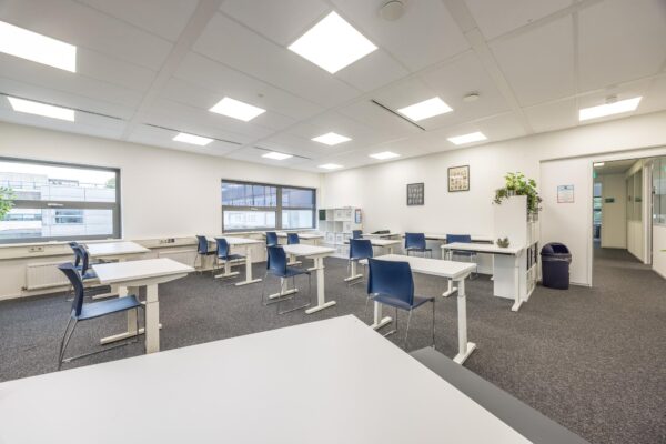 Licht en modern klaslokaal aan de Daltonlaan met losse bureaus, blauwe stoelen en grote ramen.