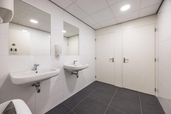 Moderne, schoon ogende openbare toiletruimte met twee wastafels, spiegels en deuren naar toiletcabines in een gebouw aan de Daltonlaan.